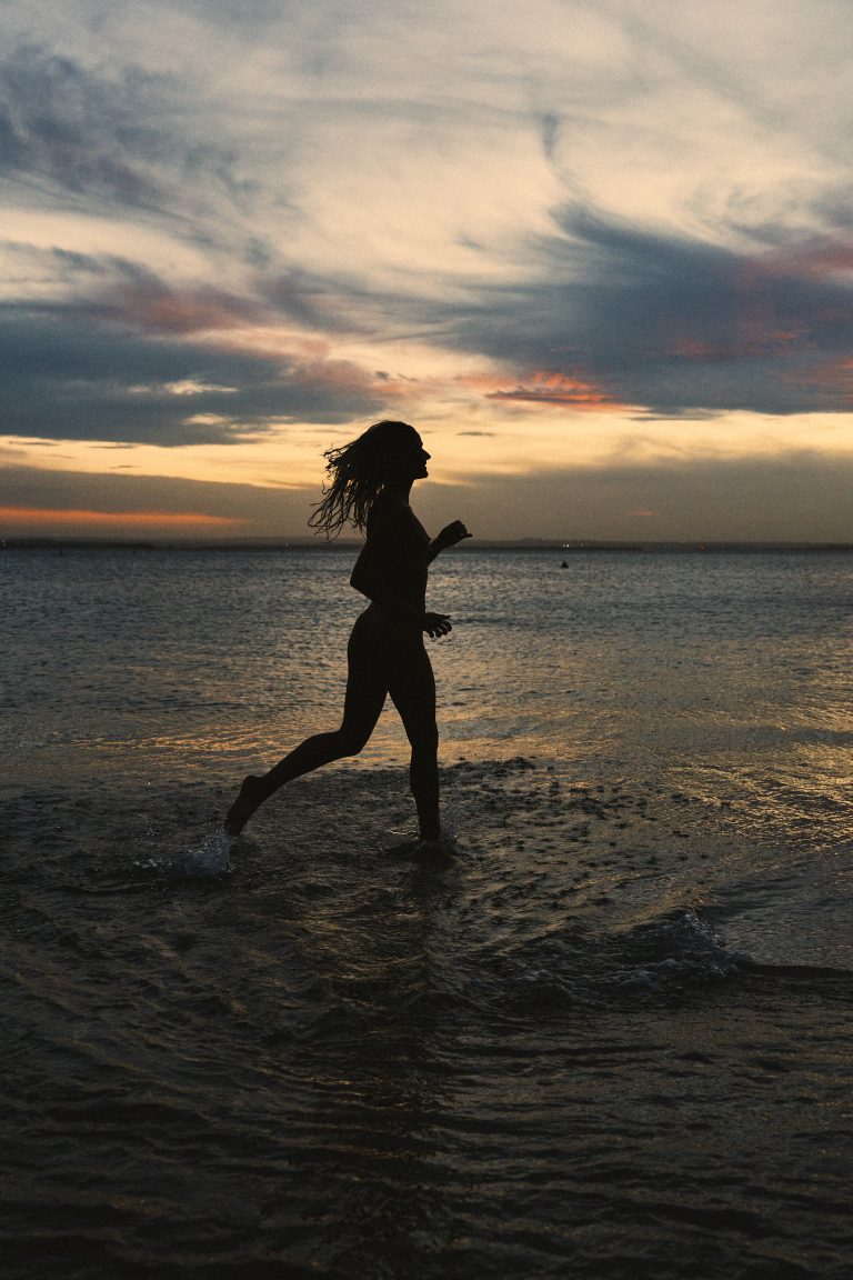 Confident empowered woman running on beach representing stepping into your power and becoming your next level self