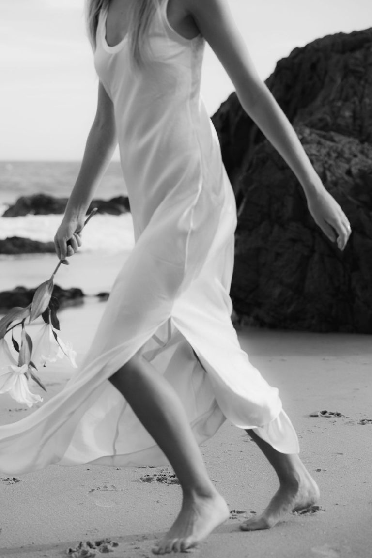 Woman running on the beach in a white dress symbolizing freedom, empowerment, and self-confidence.