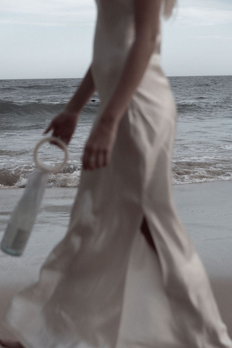 Woman walking on the beach carrying a bottle of fizz, celebrating freedom and empowerment.